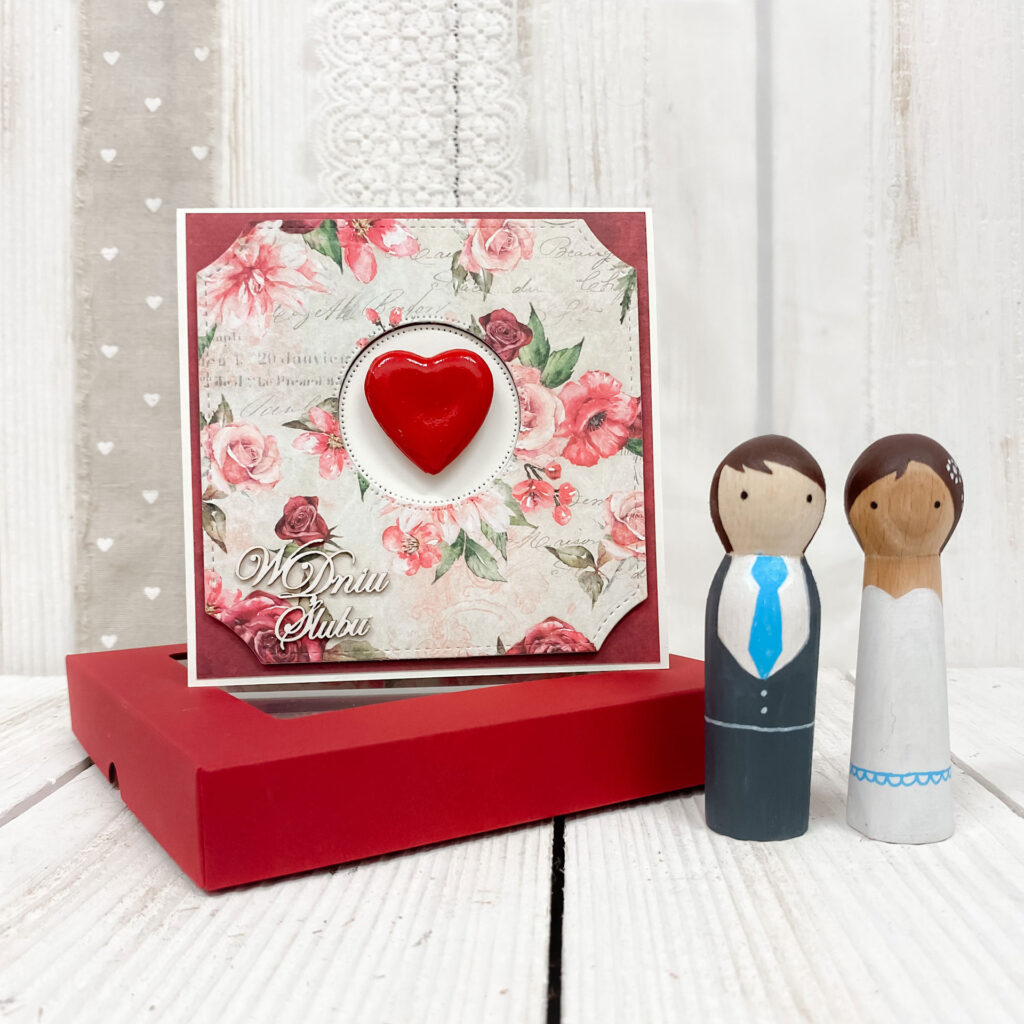 romantyczna kartka na ślub z czerwonym sercem na tle czerwonych kwiatów. z boku napis w dniu ślubu. kartka w zestawie z czerwonym pudełkiem
